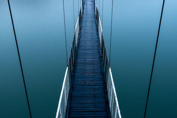 A suspension bridge fades into the mist, creating a feeling of suspense and infinity.